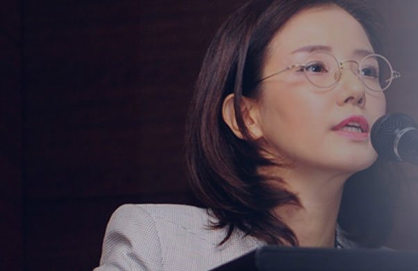 강연 중인 나민화 원장 — 안경, 회색 재킷, 마이크 앞